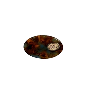 Barrette ovale en acétate écaille de tortue avec badge doré sur fond blanc pur