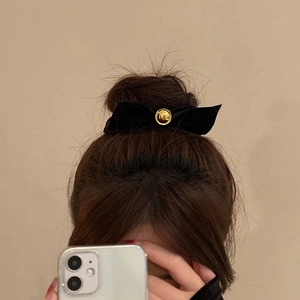 Elegant black velvet bow hair scrunchie with a gold metal accent shown on a bun
