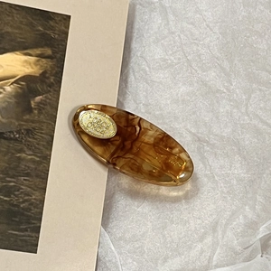 Close-up of amber tortoiseshell acetate oval hair clip with gold metal accent on white paper