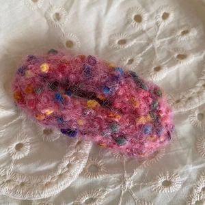 Gros plan sur la barrette nuage en tricot rose avec des mouchetures sur fond de dentelle