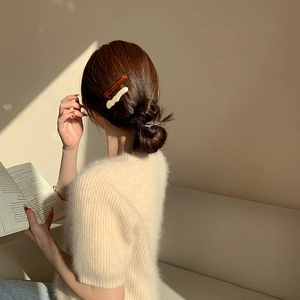 Détail de barrettes à cheveux ondulées en acrylique ambre et crème sur une queue basse
