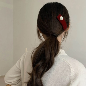Detail view of red velvet hair clip with pearl embellishment worn on low ponytail