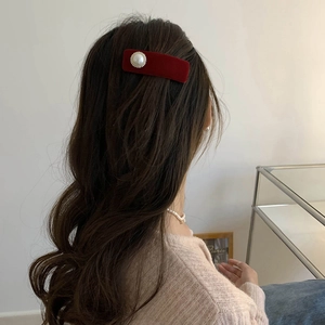 Detailed view of a red velvet hair clip with a central pearl on dark wavy hair