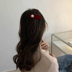 Detailed view of red velvet hair clip with a large pearl on long wavy hair