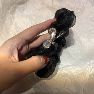 Elegant black organza hair tie with sparkling rhinestone bow detail held in hand