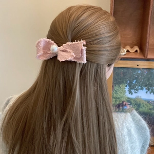 Macro detail of a pink tweed bow hair clip with a large pearl on long brown hair
