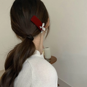 Macro shot of a red velvet hair clip with a silver rhinestone bow on model's hair
