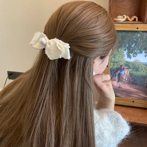 Detailed view of a white tweed bow hair clip with pearl center on a model's hair