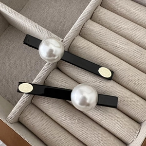 Lot de deux barrettes noires élégantes avec perles blanches et détails de logo dorés