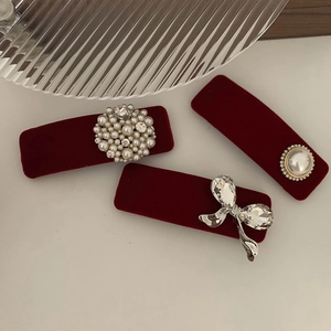 Three-piece red velvet hair clip set with pearls and crystal bow detail on beige surface