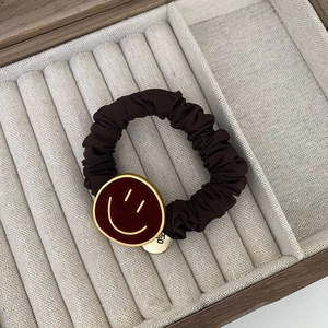 Detailopname van bruine fluwelen haarelastiek met een bordeauxrode metalen smiley