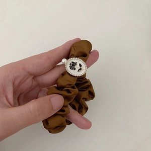 Detailed close-up of brown satin hair tie featuring a rose relief and pearl embellishment