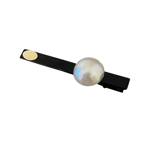 Barrette à cheveux noire minimaliste avec grande perle et étiquette dorée sur fond blanc