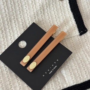 Détail de deux barrettes en acétate marron caramel avec logo doré sur tissu texturé blanc