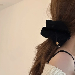 Dettaglio dell'elastico in velluto nero con ciondolo in metallo dorato sui capelli