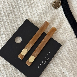 Détail de deux pinces à cheveux en acétate ambré avec des disques dorés sur tissu tweed