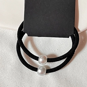 Détail de deux chouchous élastiques noirs avec perles sur fond en tissu blanc texturé