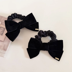 Close-up of black velvet bow hair scrunchies with elegant gold logo metal plates