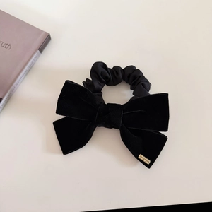 Detail of elegant black velvet hair scrunchie with a gold metal tag and large bow tie