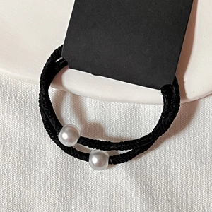 Gros plan d'un élastique à cheveux noir avec des perles argentées polies sur tissu texturé