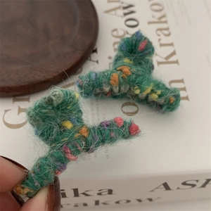 Dettaglio macro di mini molletta per capelli in maglia verde con accenti arcobaleno colorati