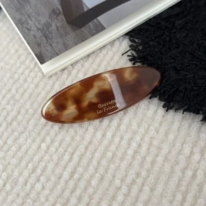 Macro shot of tortoiseshell acetate barrette with gold La France lettering on knit fabric