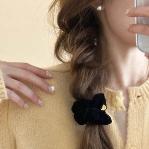 Dettaglio di scrunchie in velluto nero con emblema in metallo dorato su capelli intrecciati