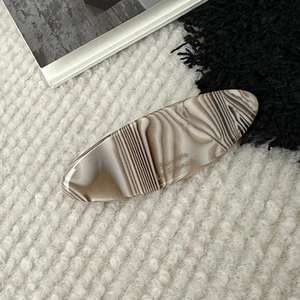 Detailed view of an oval acetate hair clip with elegant marble patterns on soft fabric
