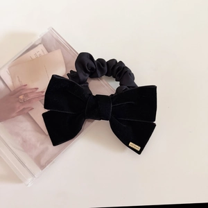 Close-up of black velvet bow hair scrunchie with a golden metal logo label engraved Lovedays