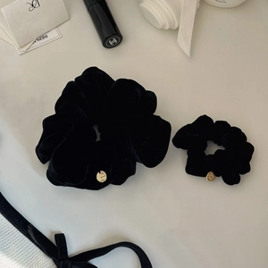 Dettaglio di due elastici in velluto nero con medagliette dorate su elegante sfondo bianco