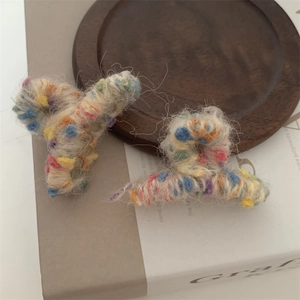 Dettaglio di mini mollette per capelli in maglia colorata su vassoio di legno