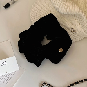 Dettaglio di elastico scrunchie in velluto nero con ciondolo in metallo dorato