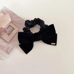 Detailed macro of a black velvet bow scrunchie with a gold metallic brand label
