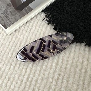 Detail shot of a large oval acetate hair clip with abstract gold foil textures on soft rug