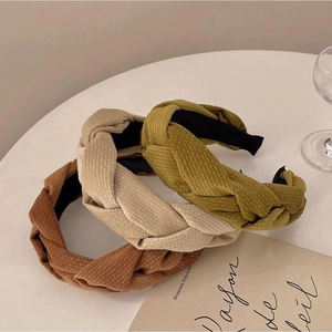 Trois serre-têtes en tissu tressé en couleurs caramel, beige et vert sur table blanche