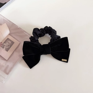 Close-up of black velvet bow hair scrunchie with gold metal logo tag detail