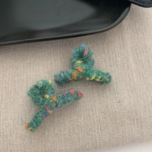 Dettaglio di mini mollette per capelli in lana verde con fibre colorate e morbida texture