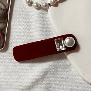 Close-up of deep red velvet hair clip featuring a clear rectangle gem and a white pearl