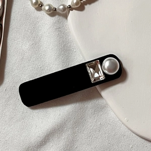 Detail of vintage black velvet hair clip with rhinestone and pearl on white fabric