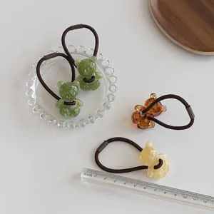 Bunte Haargummis mit Bärenanhängern und Marmormuster auf weißem Tisch mit Lineal