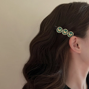 Vintage dark green hair clip with gold butterfly relief patterns worn by model