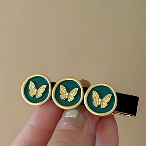 Detail of vintage metal hair clip featuring green seals with golden butterfly patterns