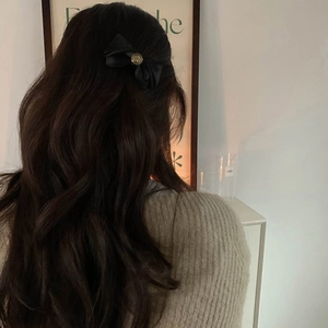 Elegant black satin bow hair clip with vintage golden relief detail on wavy brown hair