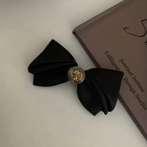 Detailed close-up of a black silk bow hair clip with a vintage gold relief button