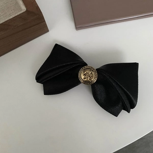 Detailed macro view of black satin bow hair clip with vintage gold coin emblem