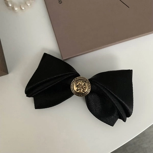 Close-up of black satin bow hair clip featuring a vintage bronze relief buckle button