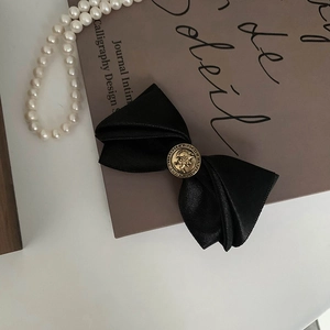 Detail of a black satin bow hair clip with an elegant golden embossed portrait coin buckle