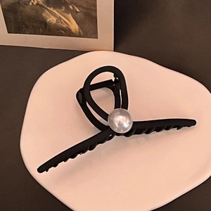 Close-up of matte black shark clip with large pearl detail on a display tray
