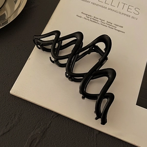 Makro-Detail einer minimalistischen mattschwarzen Wellen-Haarklammer auf Magazin