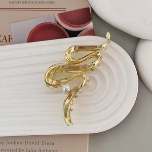 Detailed close-up of a gold metal hair claw clip with fluid lines and a pearl accent